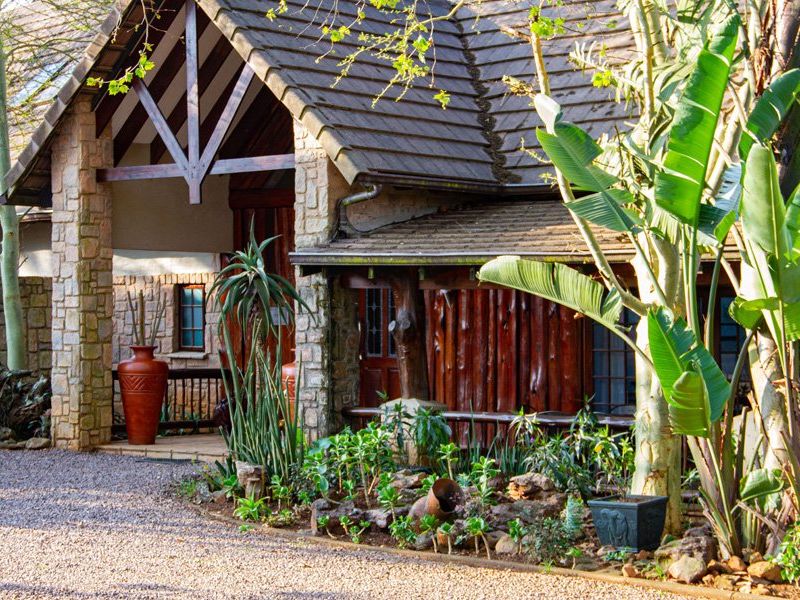 Front facade of a commercial property featuring stone and timber log exterior finishes, a pitched tiled roof, and a gravel driveway entrance.