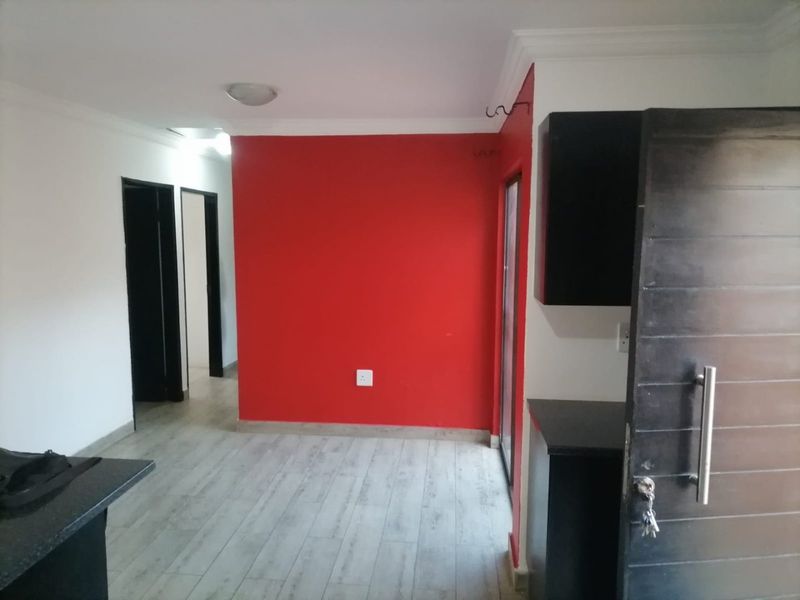 An open-plan living area featuring light laminate flooring, a bold red accent wall, and dark built-in cabinetry.