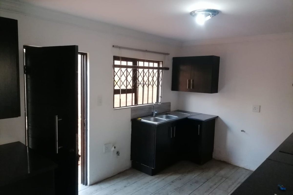 A compact kitchen featuring dark built-in cabinetry, a stainless steel sink, and laminate flooring, with direct access to an exterior door.
