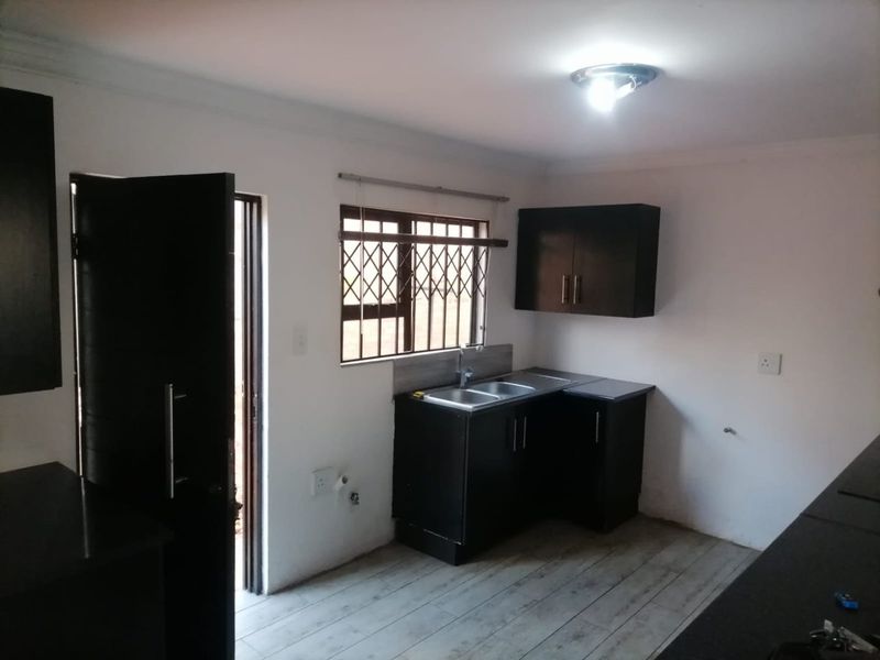 A compact kitchen featuring dark built-in cabinetry, a stainless steel sink, and laminate flooring, with direct access to an exterior door.
