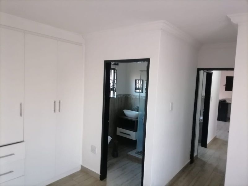 A clean, modern bedroom featuring built-in cupboards, tiled flooring, and direct access to an en-suite bathroom.