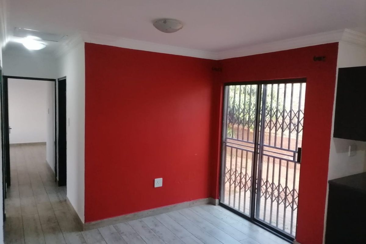 An empty living area featuring tiled flooring, a sliding glass door with security gate, and a bold red accent wall.