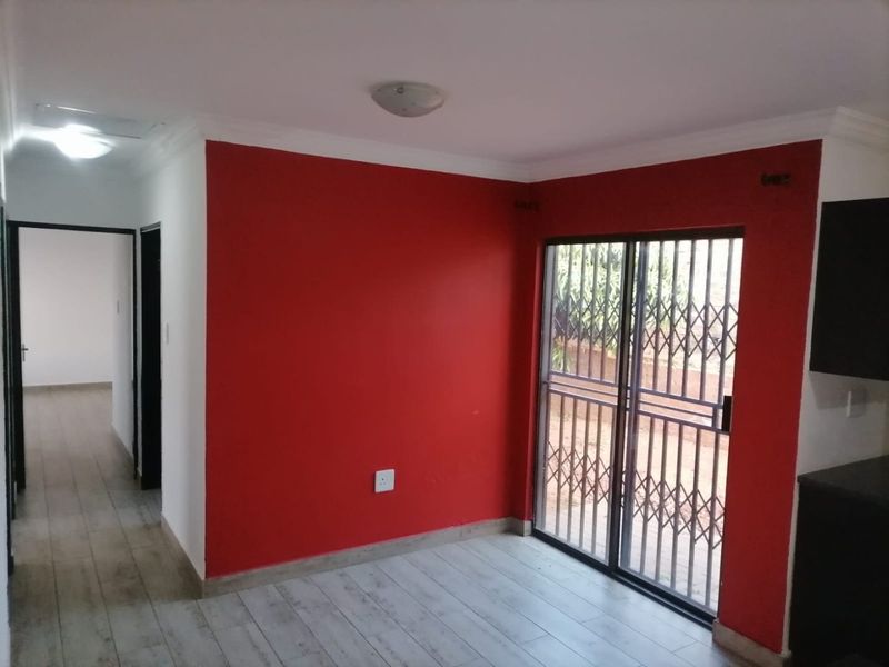 An empty living area featuring tiled flooring, a sliding glass door with security gate, and a bold red accent wall.