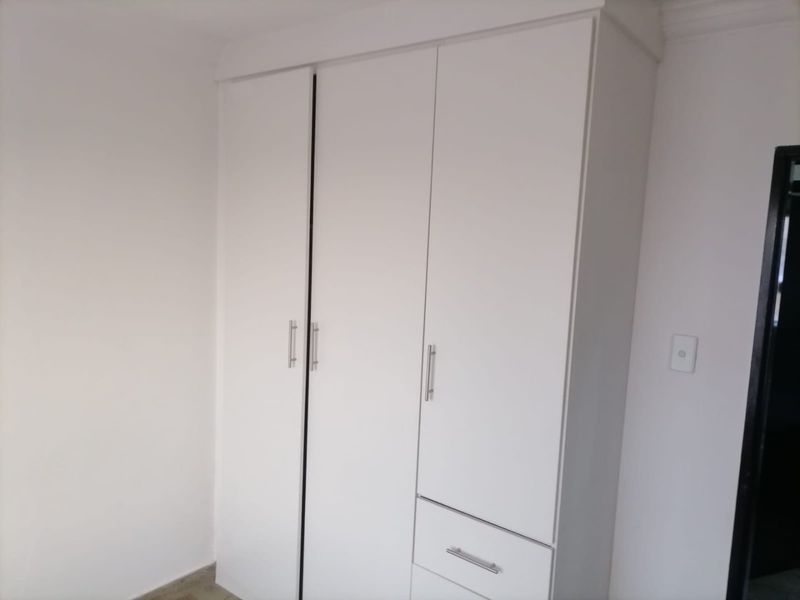 A clean, minimalist bedroom featuring a white built-in wardrobe with integrated drawer storage.
