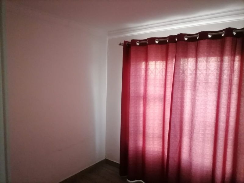 A simple, empty bedroom space featuring a window with security bars and a curtain rod.