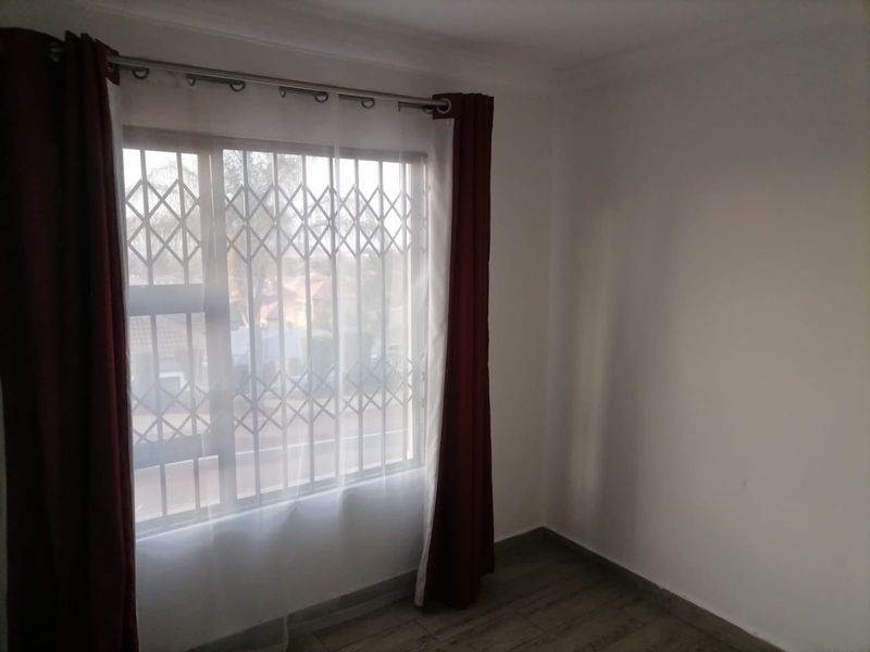 A bright, empty bedroom featuring laminate flooring and a window fitted with a security gate.