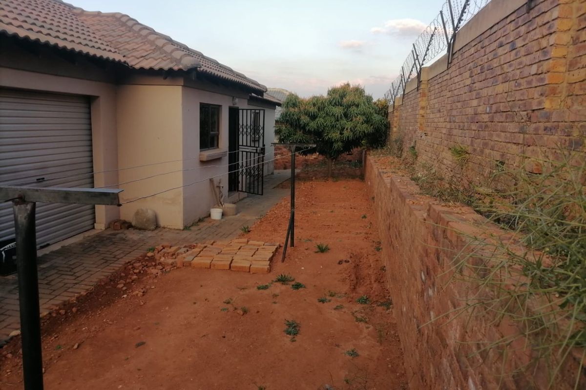 Rear exterior view showing a garage, security gate, and a large unlandscaped garden area enclosed by a high brick wall with razor wire.