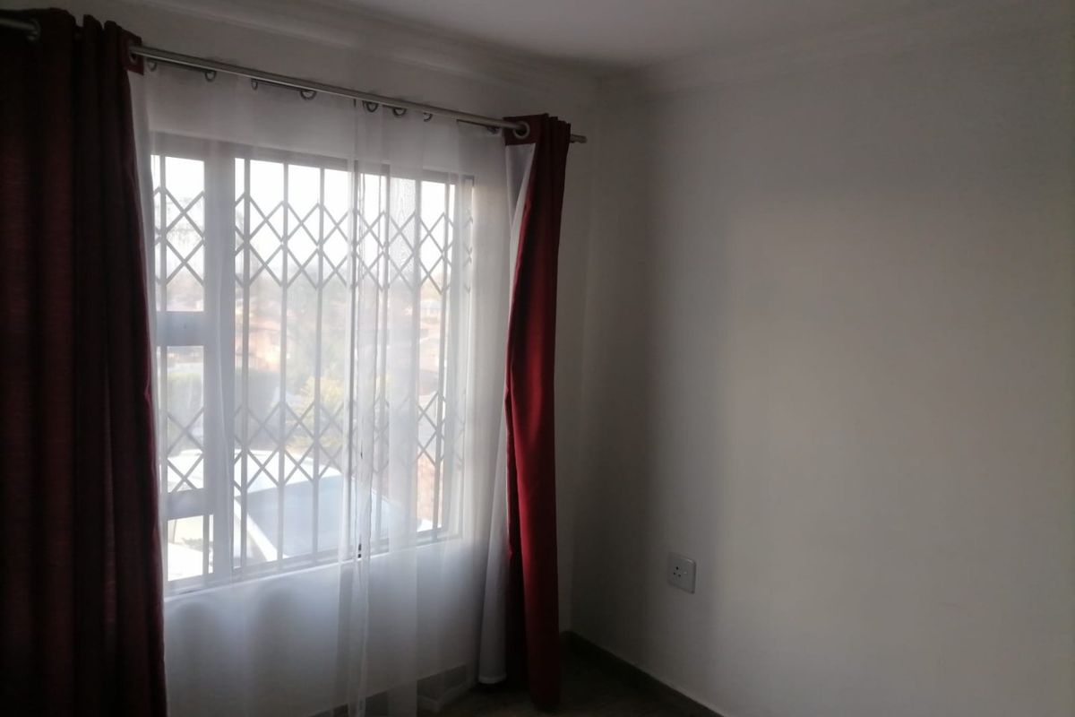 A bright, empty bedroom featuring tiled flooring, a window with a security gate, and neutral wall finishes.