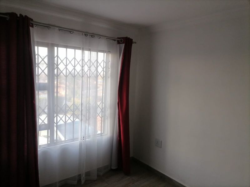 A bright, empty bedroom featuring tiled flooring, a window with a security gate, and neutral wall finishes.