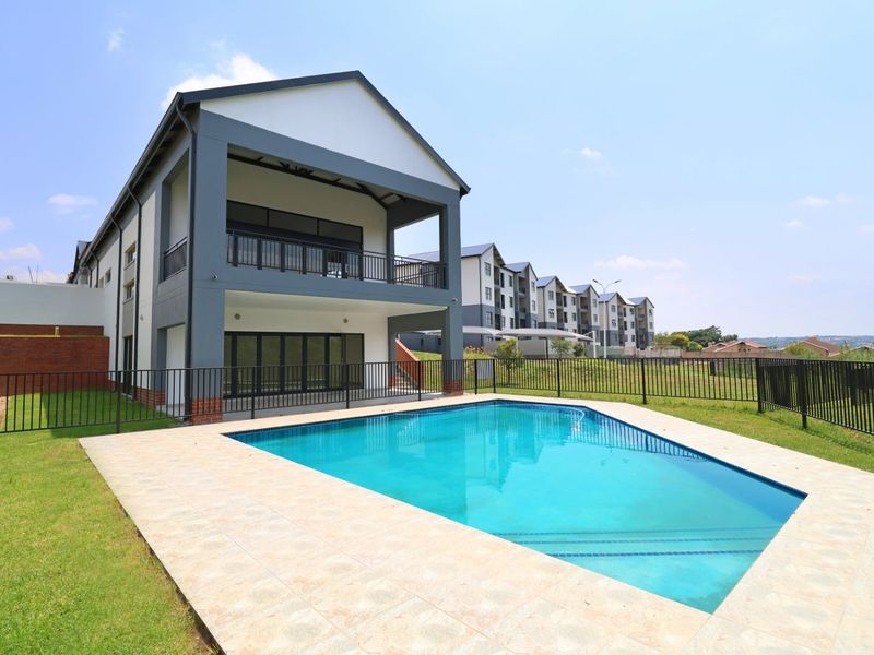 A well-maintained swimming pool area featuring a tiled surround, metal fencing, and a modern apartment building with a covered patio and balcony.