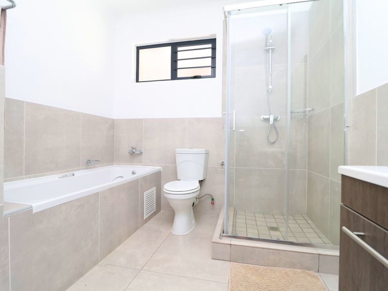 Modern bathroom featuring a built-in bathtub, separate glass shower enclosure, toilet, and vanity cabinet with neutral wall and floor tiling.