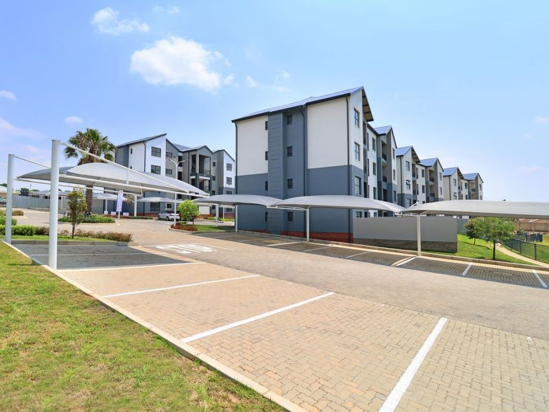 Exterior view of a modern apartment complex featuring paved parking bays with shade cloth carports and well-maintained building facades.