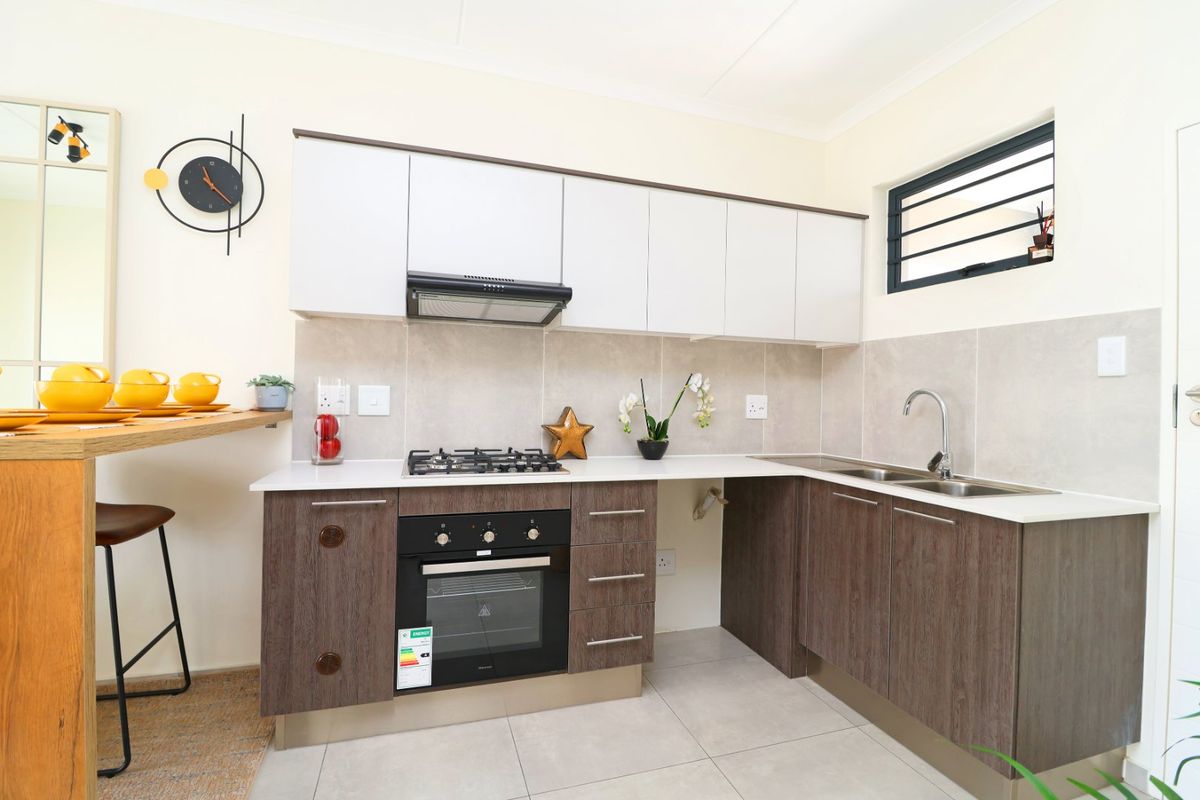 Modern kitchen featuring two-tone cabinetry, gas hob, built-in oven, extractor fan, double sink, and tiled backsplash with neutral floor tiles.