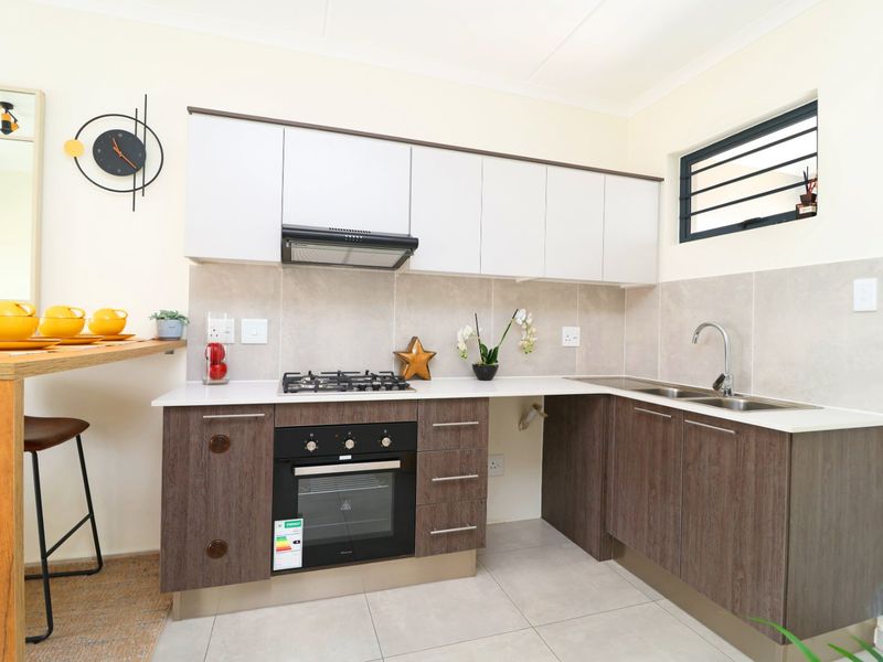 Modern kitchen featuring two-tone cabinetry, gas hob, built-in oven, extractor fan, double sink, and tiled backsplash with neutral floor tiles.