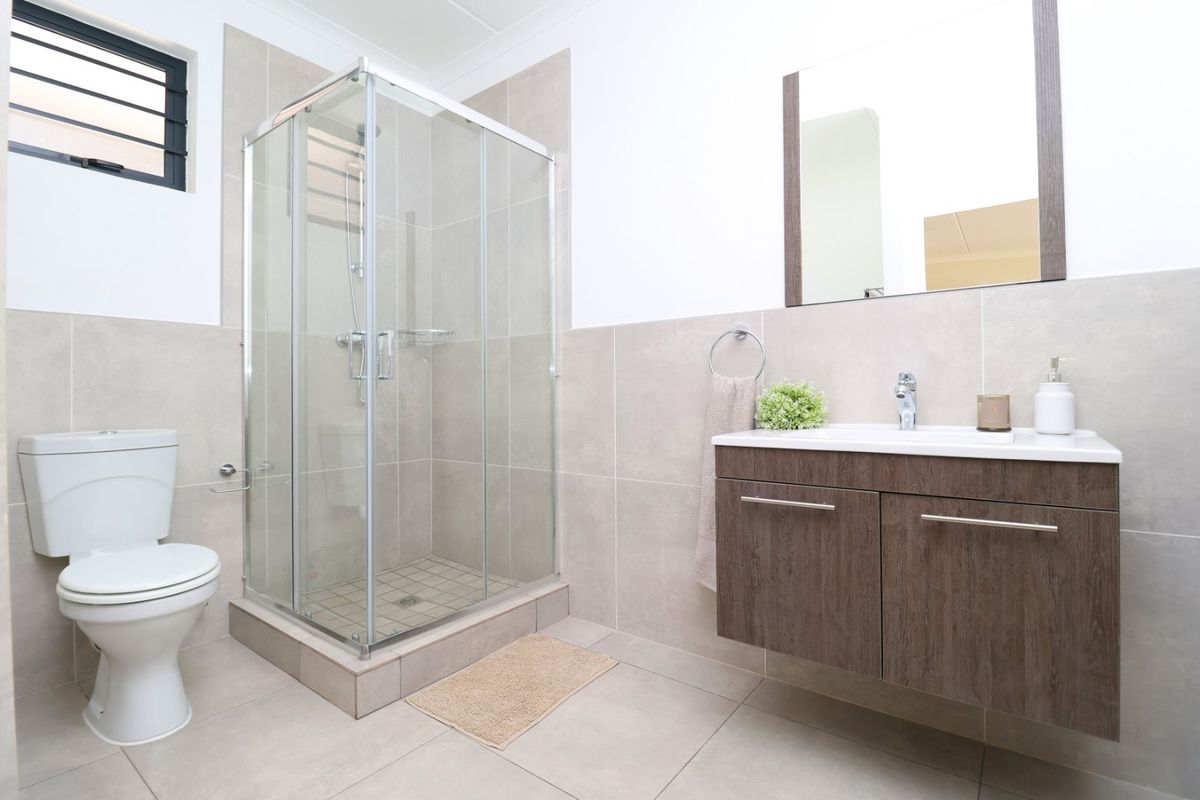 A modern bathroom featuring a glass shower enclosure, a wall-mounted vanity with a basin, and neutral floor-to-ceiling tiling.