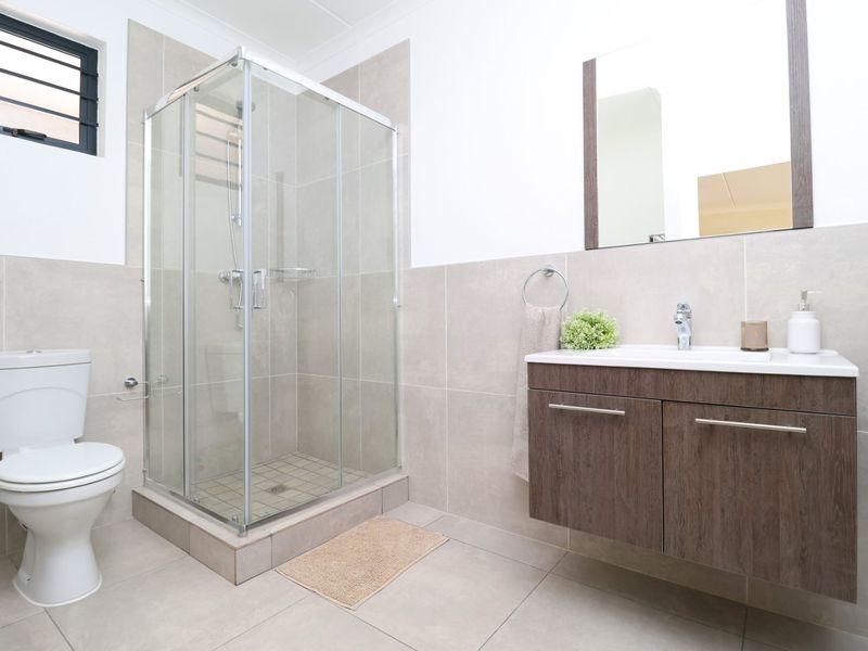 A modern bathroom featuring a glass shower enclosure, a wall-mounted vanity with a basin, and neutral floor-to-ceiling tiling.