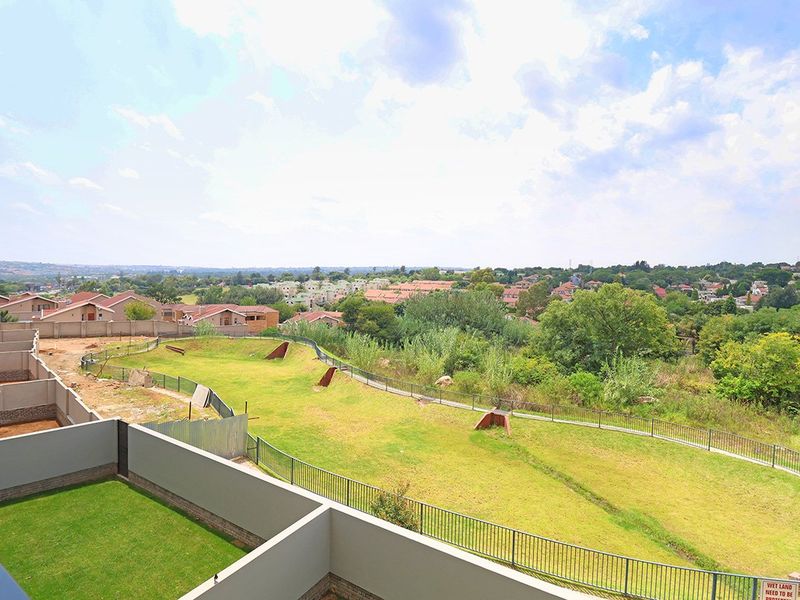 Elevated view overlooking a landscaped green belt area, perimeter fencing, and surrounding residential neighborhood.