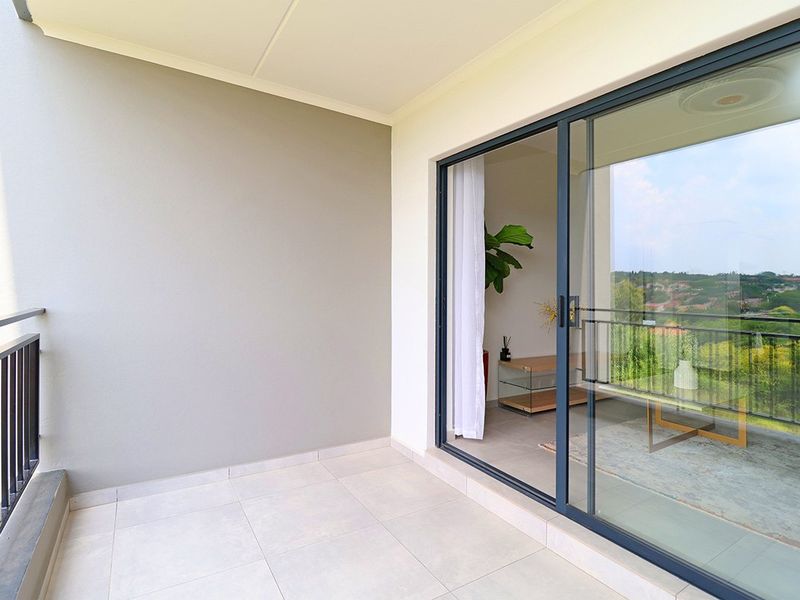 A clean, modern balcony featuring tiled flooring, a sleek metal balustrade, and large sliding glass doors providing seamless indoor-outdoor flow.