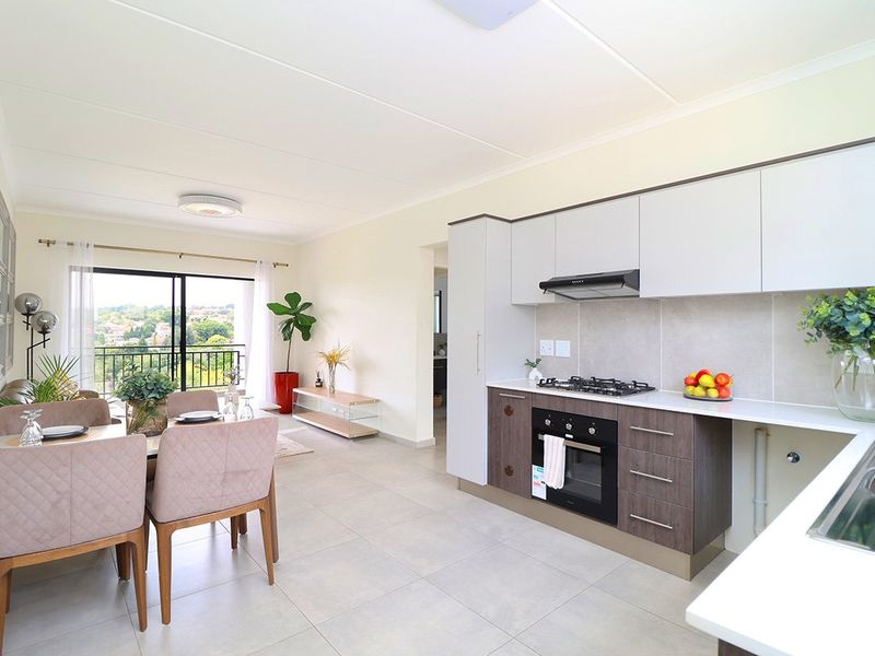 Modern open-plan kitchen and dining area featuring sleek cabinetry, built-in appliances, tiled floors, and seamless access to a balcony with scenic views.