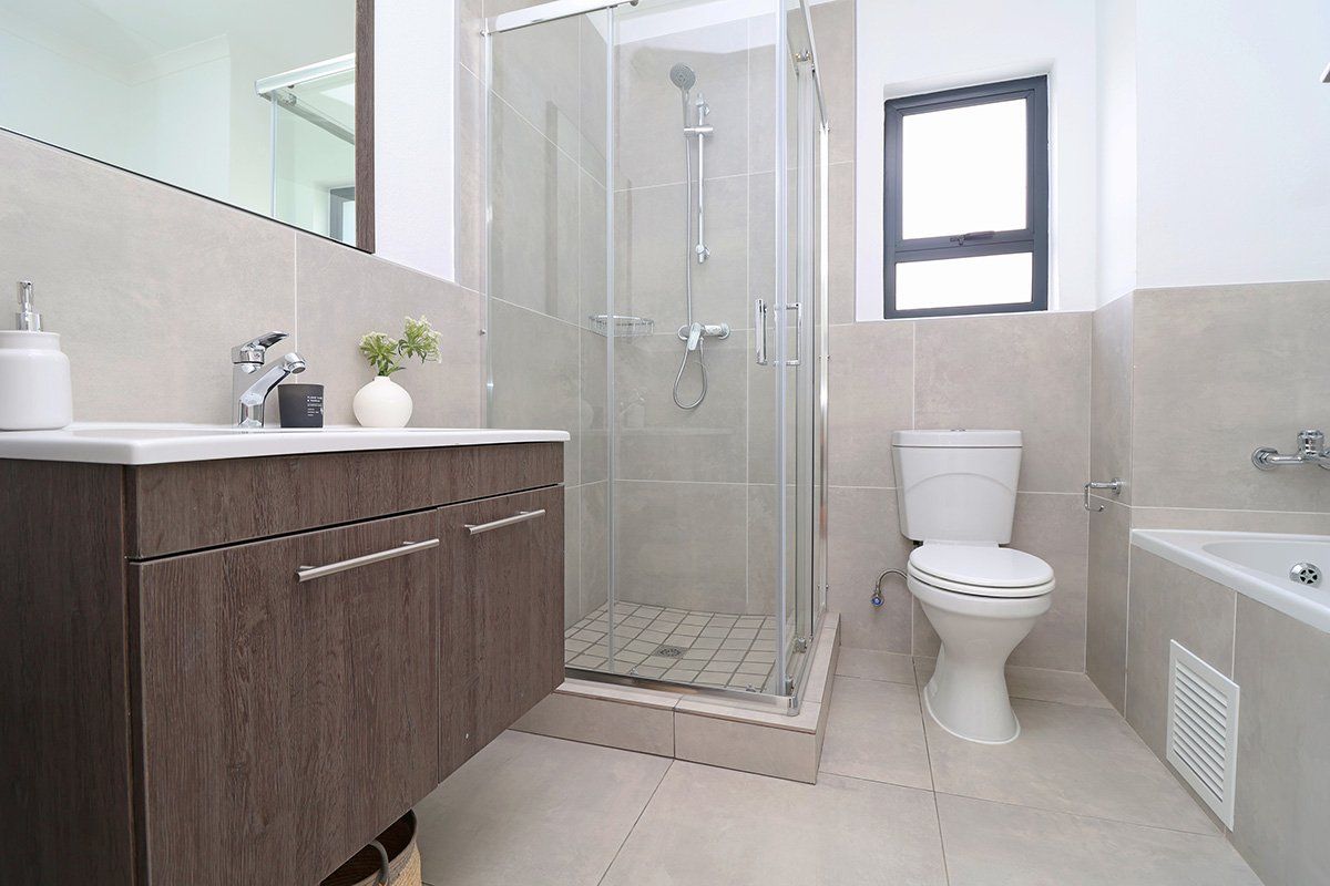 Modern bathroom featuring a vanity cabinet, glass shower enclosure, toilet, and bathtub with neutral wall and floor tiling.