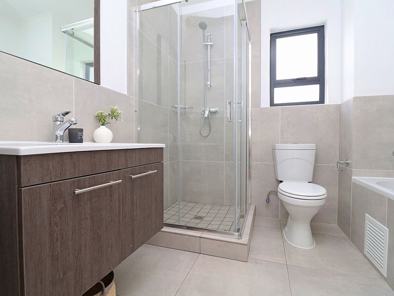 Modern bathroom featuring a vanity cabinet, glass shower enclosure, toilet, and bathtub with neutral wall and floor tiling.