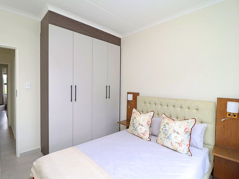 A well-maintained bedroom featuring a modern built-in wardrobe, neutral wall finishes, and tiled flooring, with integrated bedside lighting panels.