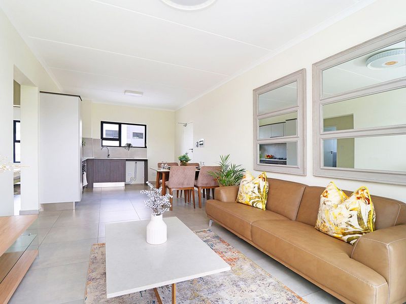 An open-plan living and kitchen area featuring neutral tiled flooring, modern cabinetry, and a functional layout suitable for contemporary apartment living.