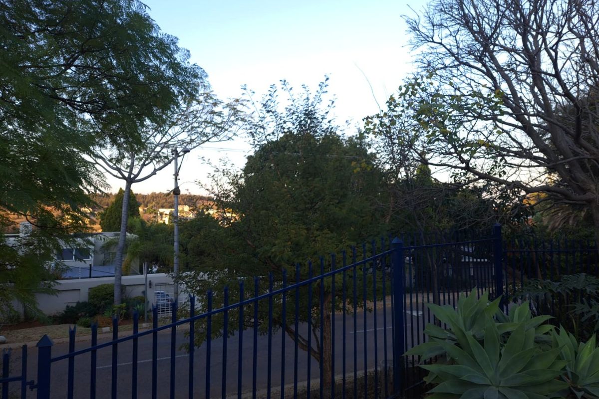 A view of the street frontage featuring established trees and secure metal perimeter fencing.