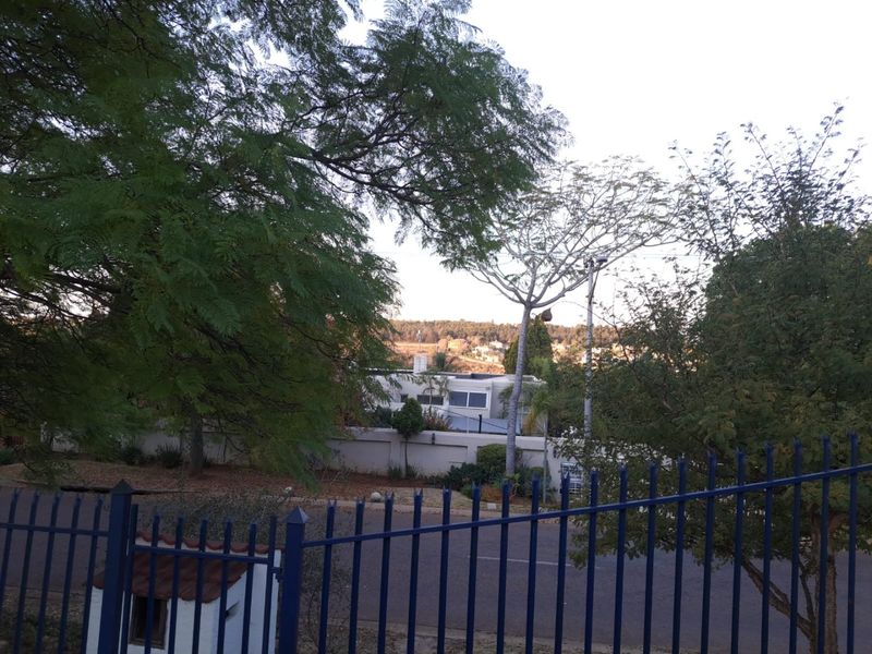 A street-level view of the property frontage, featuring established trees, a boundary wall, and metal perimeter fencing.