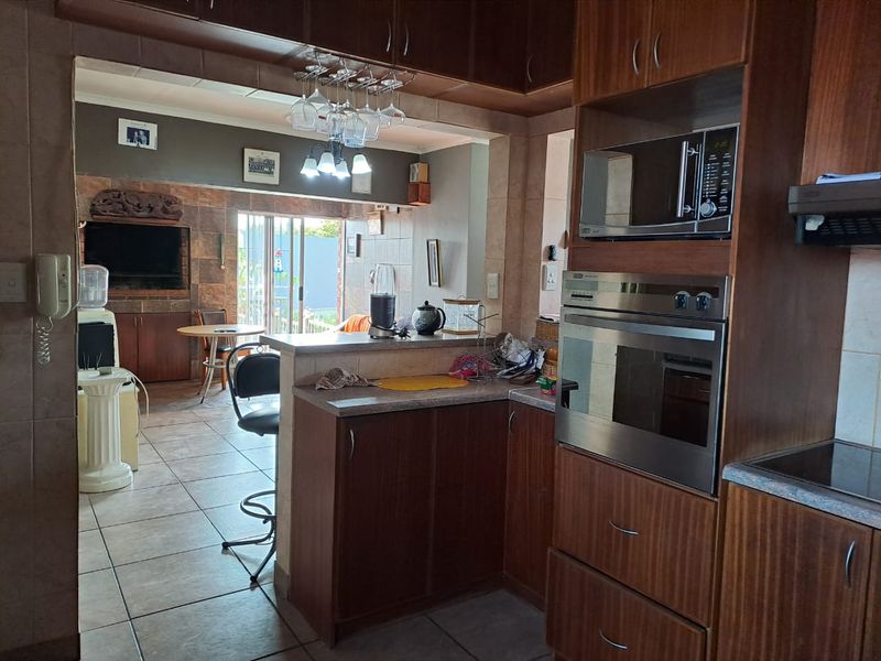 Open-plan kitchen and living area featuring dark wood cabinetry, built-in appliances, tiled flooring, and a breakfast bar connecting to the adjacent living space.