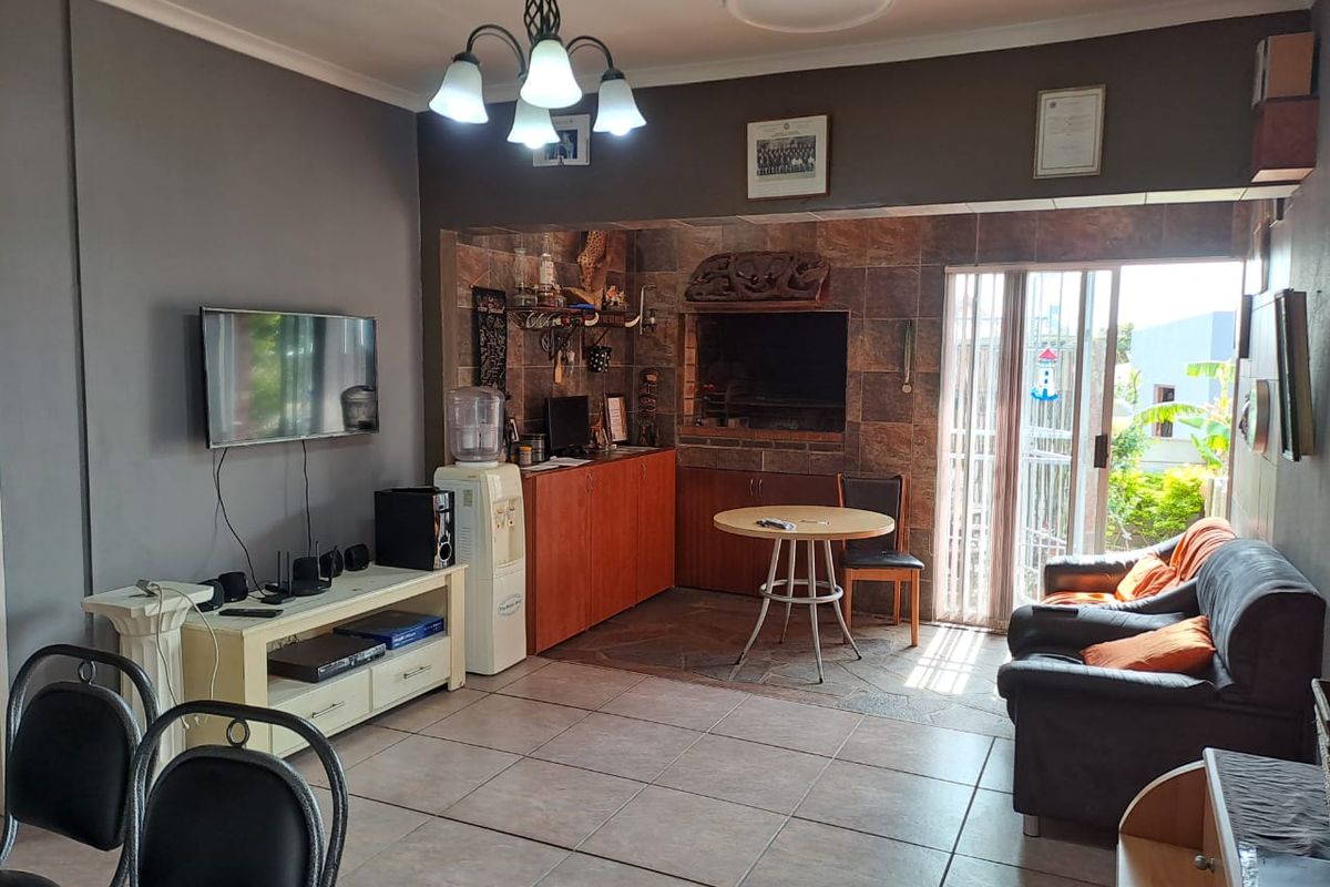 A living area featuring tiled flooring, a built-in braai with stone-tiled surround, and sliding glass doors providing access to the outdoor space.