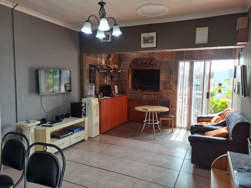 A living area featuring tiled flooring, a built-in braai with stone-tiled surround, and sliding glass doors providing access to the outdoor space.