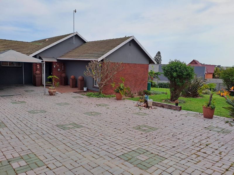 Front view of a residential house featuring a paved driveway, brick and rendered facade, tiled roof, and a landscaped garden area.