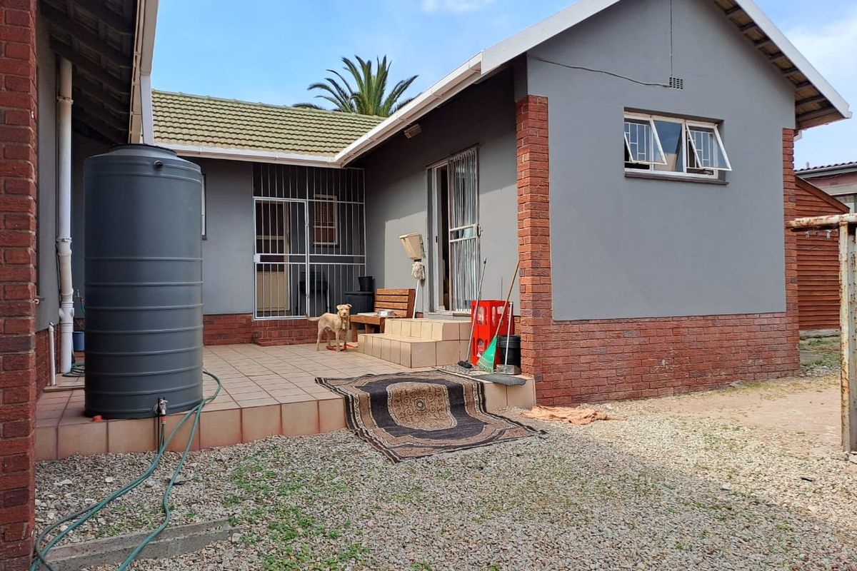 Rear exterior view of the house featuring a tiled patio area, a water storage tank, and brick and plaster wall finishes.