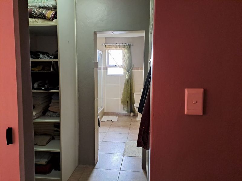 A view through a doorway into a bathroom featuring tiled floors, a shower enclosure, and a toilet, adjacent to a built-in storage closet.