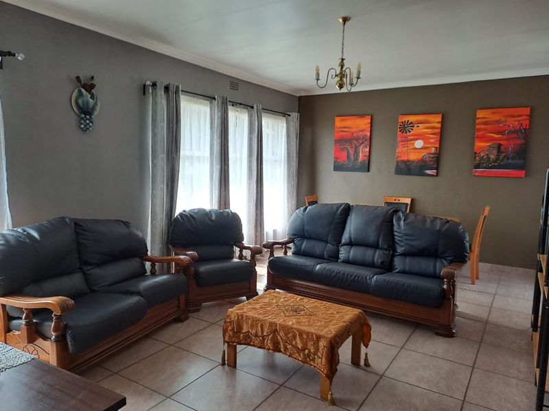 A spacious living room featuring neutral tiled flooring, large windows with curtain tracks, and a central ceiling light fixture.