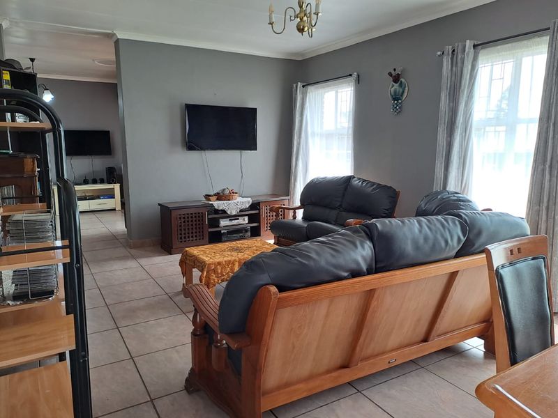 A spacious living room featuring neutral grey walls, ceramic tile flooring, and large windows with security bars, offering a comfortable and functional living space.