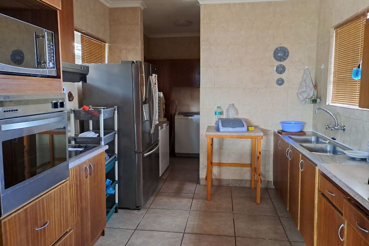 A functional kitchen featuring wood-finish cabinetry, built-in oven and microwave, tiled walls, and a double sink with a view into the adjacent laundry area.