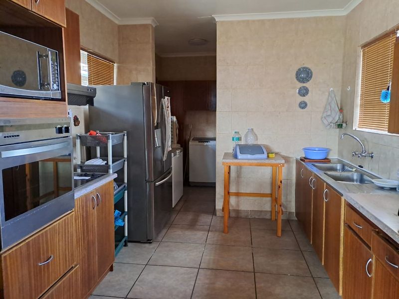 A functional kitchen featuring wood-finish cabinetry, built-in oven and microwave, tiled walls, and a double sink with a view into the adjacent laundry area.