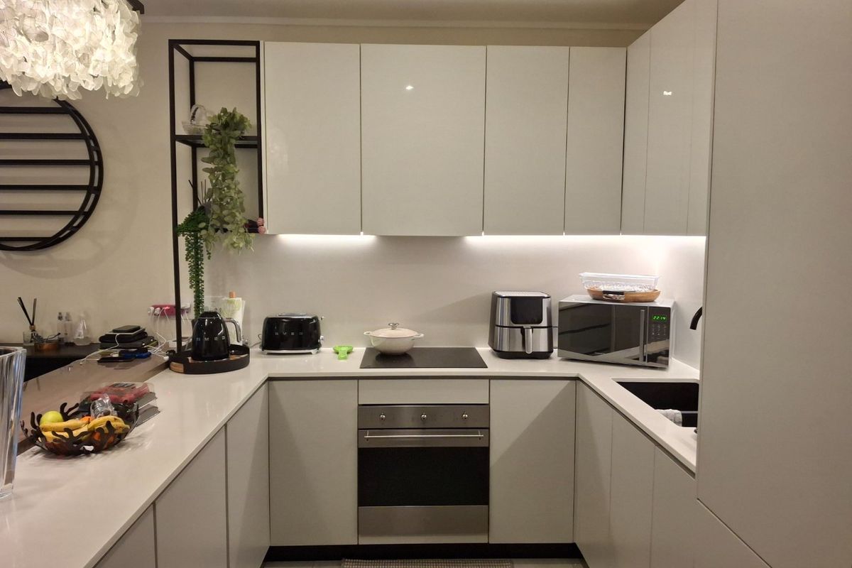 Modern U-shaped kitchen featuring sleek white cabinetry, quartz countertops, integrated appliances, and ambient under-cabinet lighting.