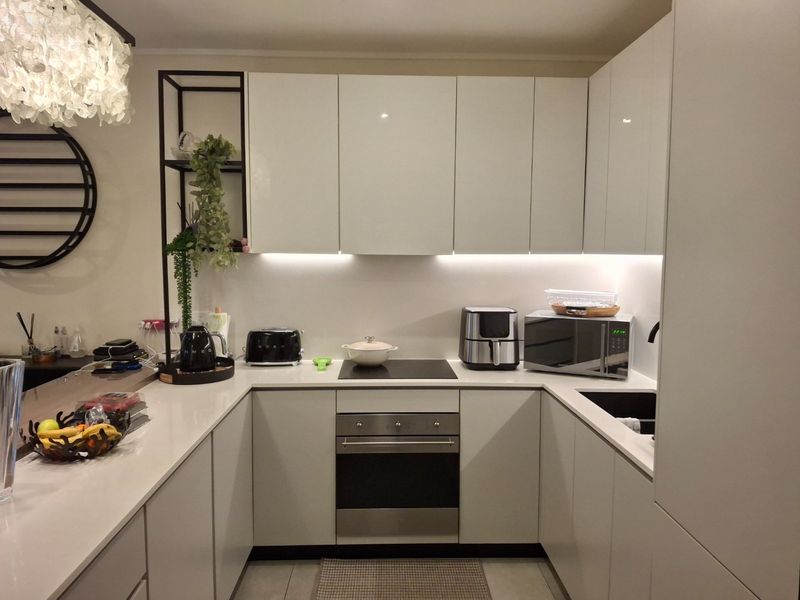 Modern U-shaped kitchen featuring sleek white cabinetry, quartz countertops, integrated appliances, and ambient under-cabinet lighting.