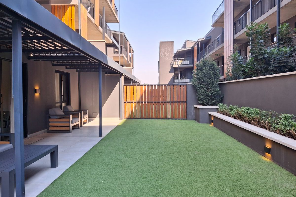 A well-maintained private rear courtyard featuring a covered patio area, artificial lawn, and integrated garden lighting within a modern apartment complex.