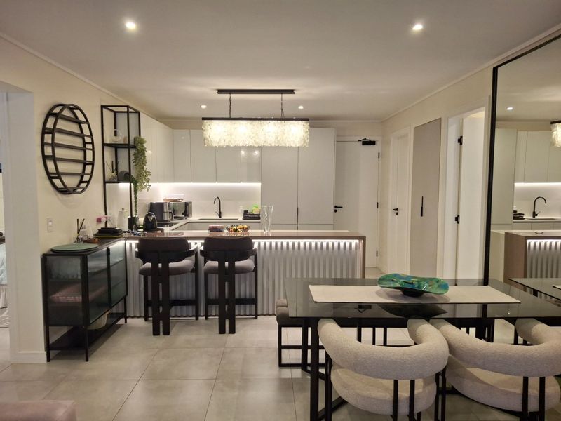 Modern open-plan kitchen and dining area featuring sleek cabinetry, a central island with integrated lighting, and contemporary tiled flooring.