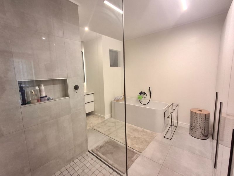 Modern bathroom featuring a freestanding bathtub, a spacious walk-in shower with a glass screen, a recessed niche, and a sleek vanity unit.