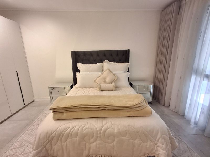 A well-maintained bedroom featuring neutral tiled flooring, a built-in wardrobe, and floor-to-ceiling curtains providing ample natural light.