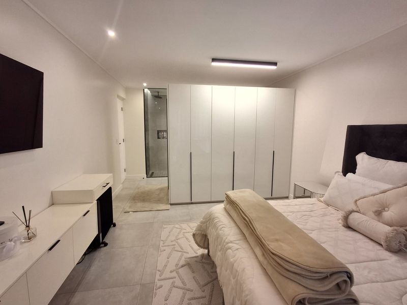 Modern bedroom featuring sleek built-in cupboards, tiled flooring, recessed lighting, and an integrated en-suite shower area.