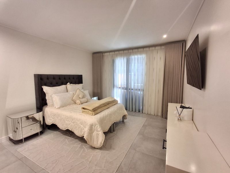 A well-maintained bedroom featuring neutral tiled flooring, recessed lighting, and large sliding glass doors with floor-to-ceiling curtains providing access to the exterior.