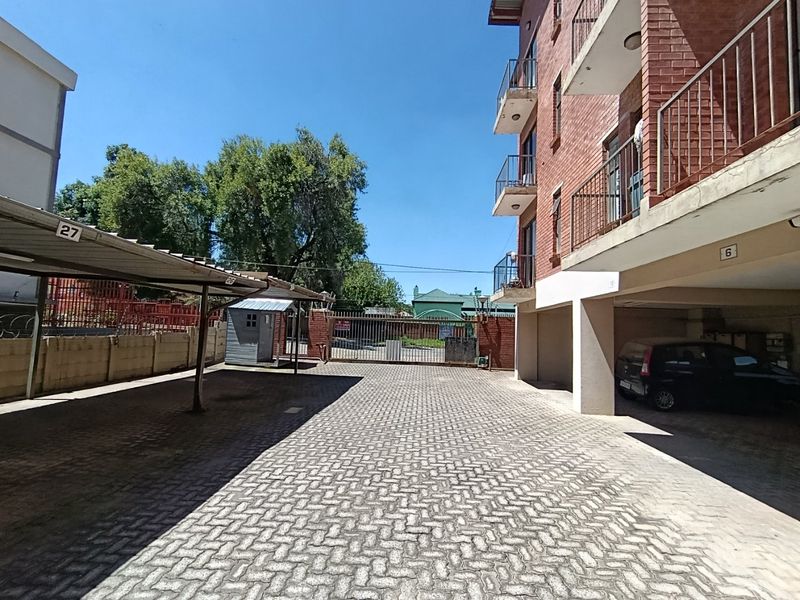 Exterior view of the apartment complex showing the paved parking area, covered parking bays, and the brick building facade with balconies.
