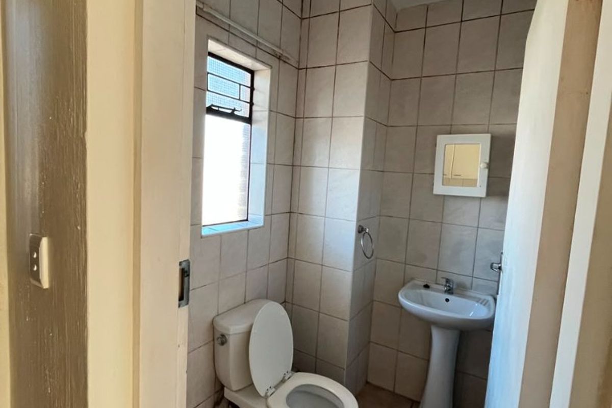 A compact bathroom featuring a pedestal washbasin, toilet, and neutral wall and floor tiling, requiring minor cosmetic updates.