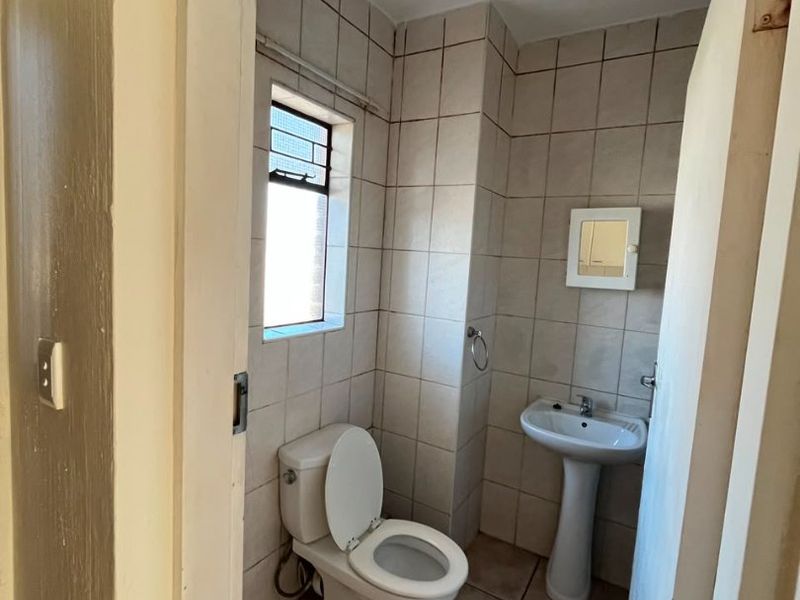 A compact bathroom featuring a pedestal washbasin, toilet, and neutral wall and floor tiling, requiring minor cosmetic updates.